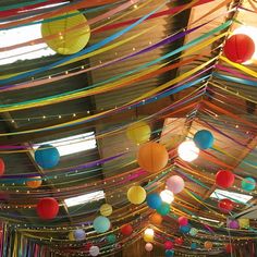 many colorful paper lanterns hanging from the ceiling in a room filled with lights and streamers