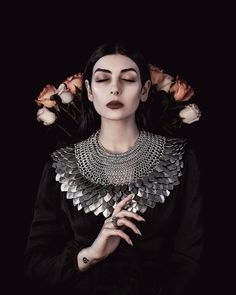 a woman with flowers in her hair wearing a black dress and silver statemented necklace