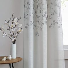 a white vase with flowers on a table next to a window