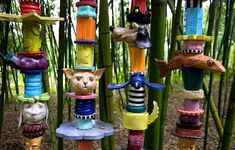 a bunch of cat figurines that are hanging on some bamboo poles in the woods