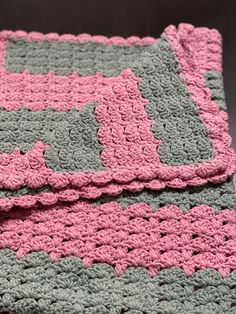 a crocheted blanket with pink and gray squares on it, folded over the edge