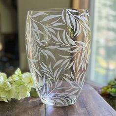 a clear glass sitting on top of a wooden table next to green plants and flowers