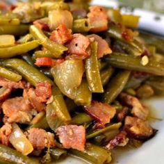 green beans and bacon are piled together on a white plate with a fork in the background