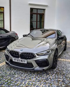 two bmw cars parked next to each other on a cobblestone street in front of a white building