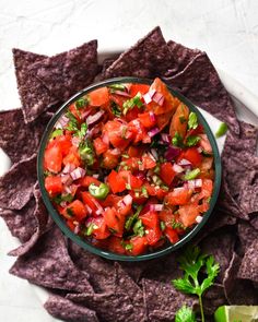 a bowl of salsa surrounded by tortilla chips and cilantro wedges