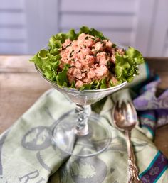 a glass bowl filled with lettuce and meat on top of a wooden table