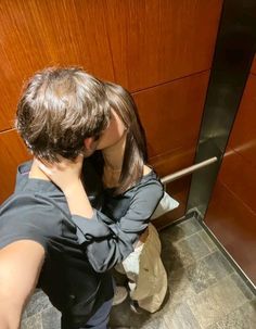 a man and woman kissing in front of an elevator door with their hands on each other's backs