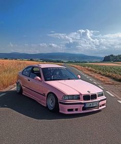 the pink car is parked on the side of the road in front of an open field