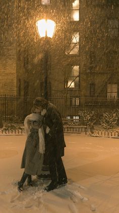 a man and woman are kissing in the snow at night with a street light behind them