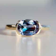 "This beautiful oval lab grown color change sapphire ring was made of 8mmx6mm oval sapphire stone in 14k gold half bezel  bezel setting and 14k yellow gold 2mm hammered band.  It's perfect as a solitaire engagement ring or statement ring. DETAILS  Ring Band: 14K YELLOW GOLD Ring Band size: 2mm wide x 1mm thick half round Ring Band is hammered or smooth by requested. Gemstone: Lab grown color change sapphire Gemstone size and cut: 6x8mm oval cut Carat weight  : 1.25 ct. weight Gemstone Quality : AAA      All our raw materials are sourced from US-based companies for the quality and safety of our handmade products.  this ring is handcrafted for you in our local studio in Redlands, California. We are a small workshop which specializes on handmade jewelry.  All orders are elegantly packaged in Color Change Sapphire, Oval Sapphire Ring, Half Bezel, Hammered Band, Sapphire Engagement Ring, Local Jewelry, Detailed Ring, Purple Band, Sapphire Stone