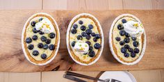 three desserts with blueberries and whipped cream on them sitting on a cutting board