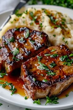 two pieces of meat and mashed potatoes on a white plate with garnish