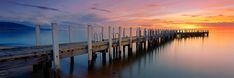 a long wooden pier sitting on top of a lake under a cloudy sky at sunset