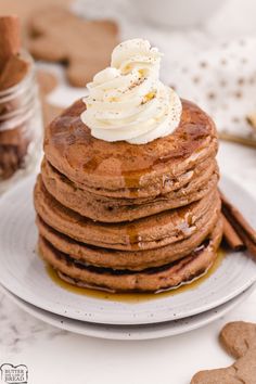 a stack of pancakes with whipped cream on top and cinnamon sticks next to it, sitting on a white plate