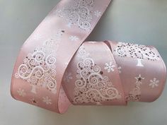 a pink ribbon with white lace and snowflakes is on a gray surface,