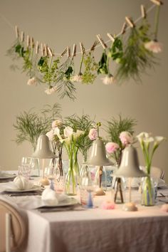 the table is set with flowers, candles and vases hanging from strings above it