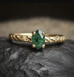 a close up of a ring on a rock with a green stone in the middle