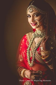 a woman in a red and gold bridal outfit with jewelry on her head, posing for the camera