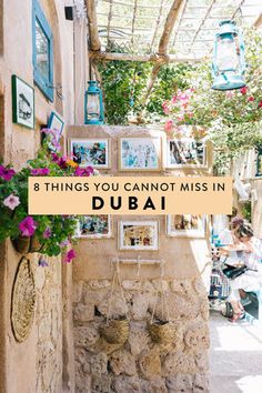 an alleyway with flowers and pictures hanging on the wall, text overlay reads 8 things you cannot miss in dubai