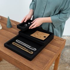 a woman standing next to a wooden table with jewelry on it and an object in the middle