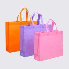 three different colored shopping bags on a white background with one pink, one orange and one purple