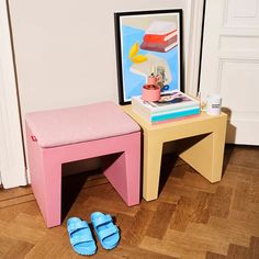 a pair of blue slippers sitting on top of a wooden table next to a pink stool