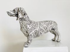 a sculpture of a dog made out of newspaper strips on a white pedestal with a gray background