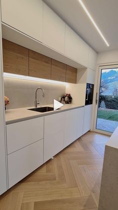 an empty kitchen with white cabinets and wood flooring on the walls, along with a sliding glass door that leads to a patio