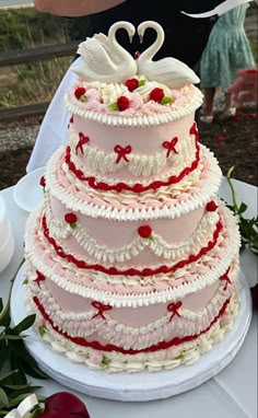 a three tiered wedding cake with swans on top and roses around the edges, is ready to be cut