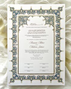 an ornate wedding card with blue and gold trimmings on white paper, surrounded by flowers