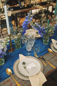 the table is set with blue and white flowers, silverware, and napkins