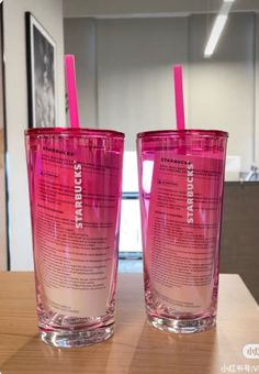 two pink tumblers sitting next to each other on a wooden table in an office