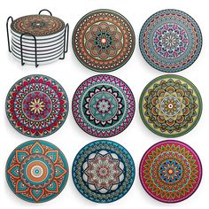 six colorful plates with designs on them sitting in front of a wire rack and plate holder