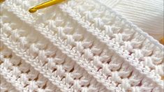 a crocheted white blanket with a gold knitting needle on the end of it