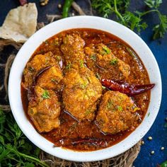 a white bowl filled with meatballs covered in sauce and garnished with parsley