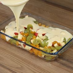 a person pouring dressing into a casserole filled with fruit and vegetables on a wooden table