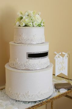 a three tiered wedding cake with white flowers on top and a card holder in the middle