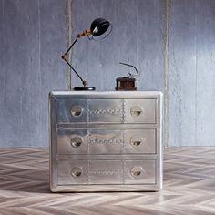 a metal dresser with two drawers and a lamp on top, in front of a wall