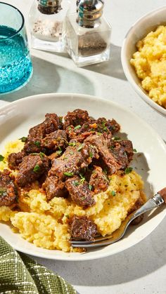 a white plate topped with meat and mashed potatoes next to a glass of water