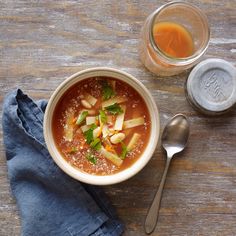 a bowl of soup on a wooden table next to a spoon and glass with liquid in it