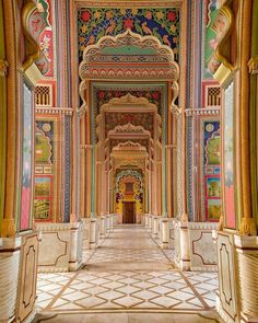 an ornate hallway with colorful painted walls and columns on either side, leading to a doorway