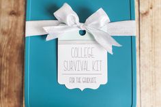 a teal box with a white ribbon tied around it and a tag that says college survival kit for the graduate