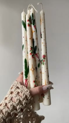 a person holding four white candles in their hand with holly decorations on them, all wrapped up and ready to be lit