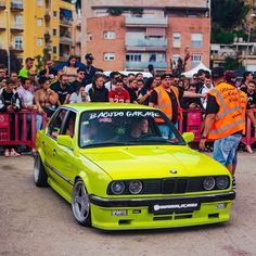 a yellow car is parked in front of a group of people with orange vests