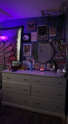 a bedroom with purple lighting and pictures on the wall, dresser in front of it