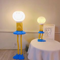 two yellow and blue lamps with faces on them sitting on top of a white table