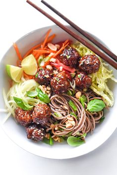 a white bowl filled with meatballs and veggies next to chopsticks