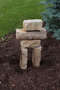 a stone sculpture sitting on top of a pile of mulch next to a tree