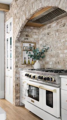 a white stove top oven sitting inside of a kitchen next to a brick wall with an arched doorway