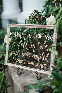 a mirror with writing on it sitting in front of some bushes and trees, next to a potted plant